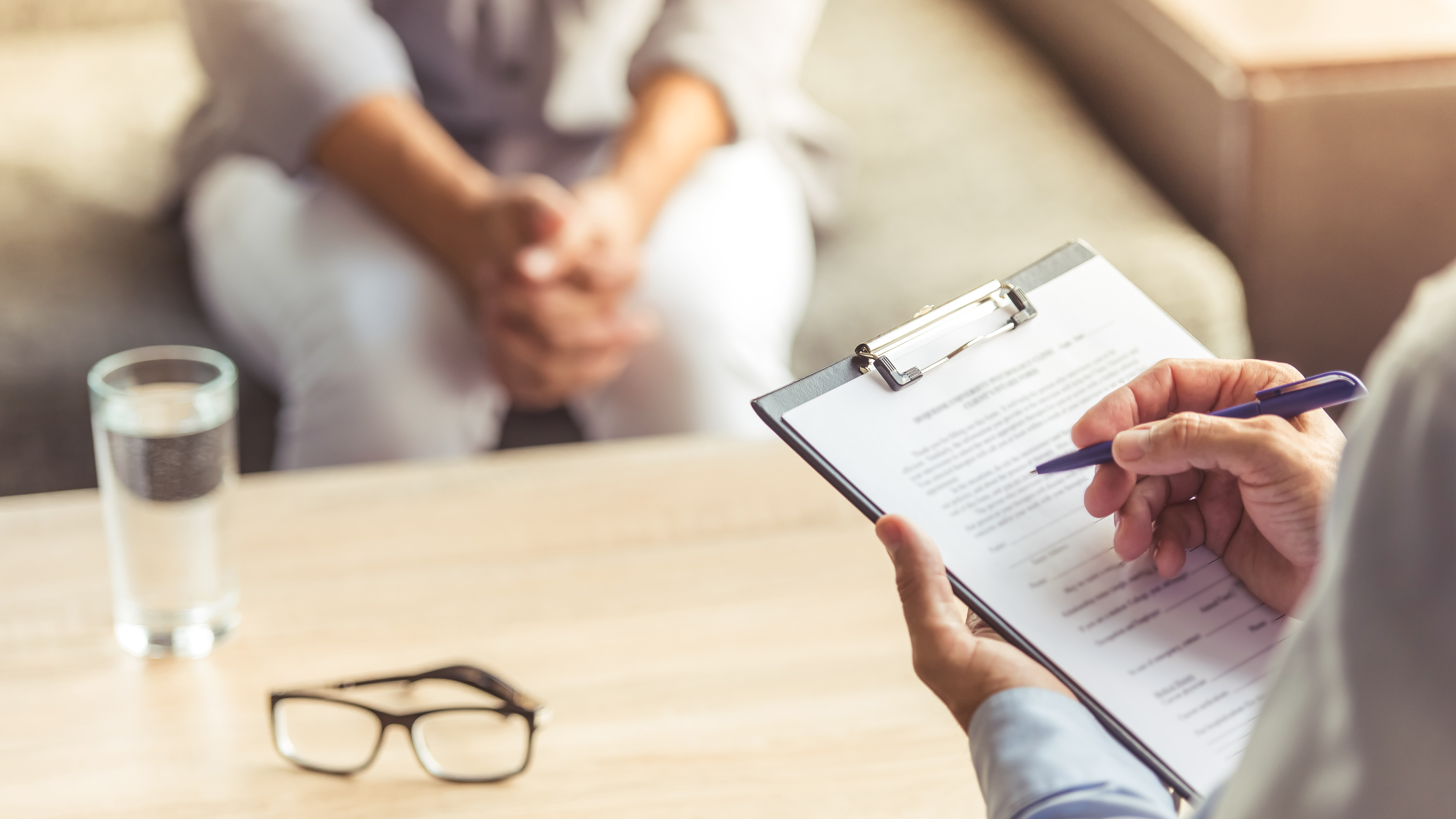 Cropped image of depressed man at the psychotherapist. Doctor is making notes while listening to his patient